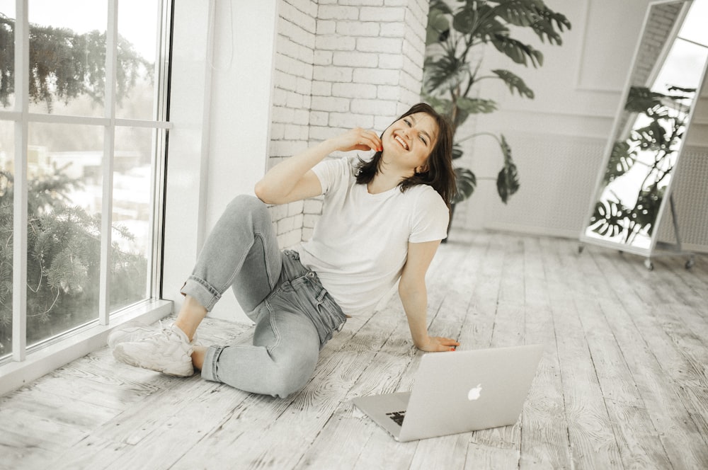 woman in white shirt and blue denim jeans sitting on floor using macbook
