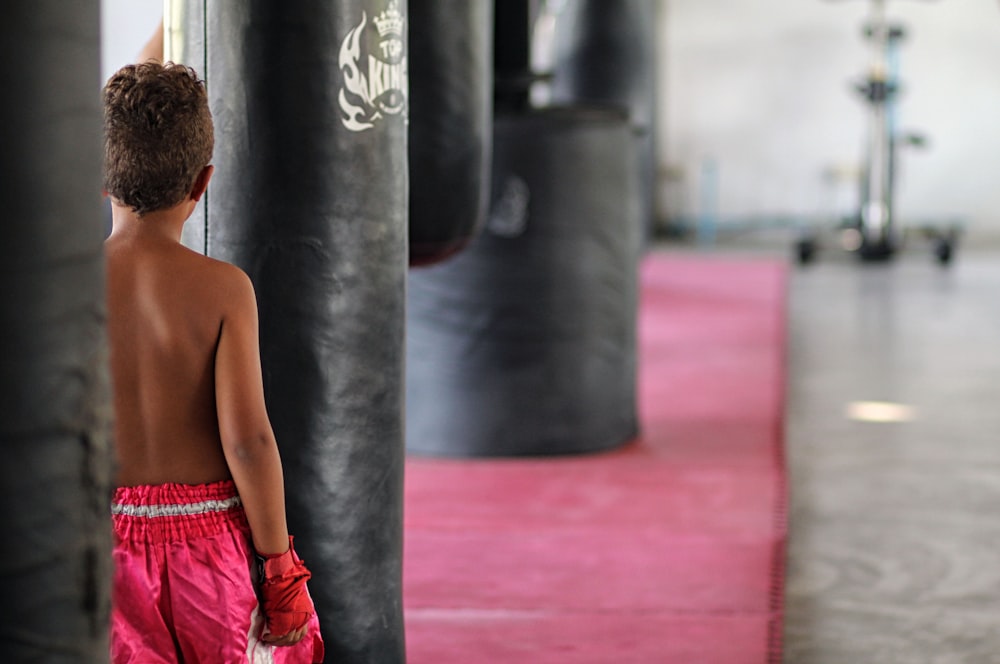 topless boy in red shorts standing near black and gray exercise equipment