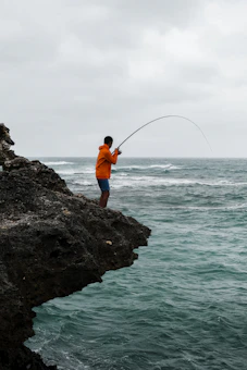 Angler casting a sea rod from the shore during daytime