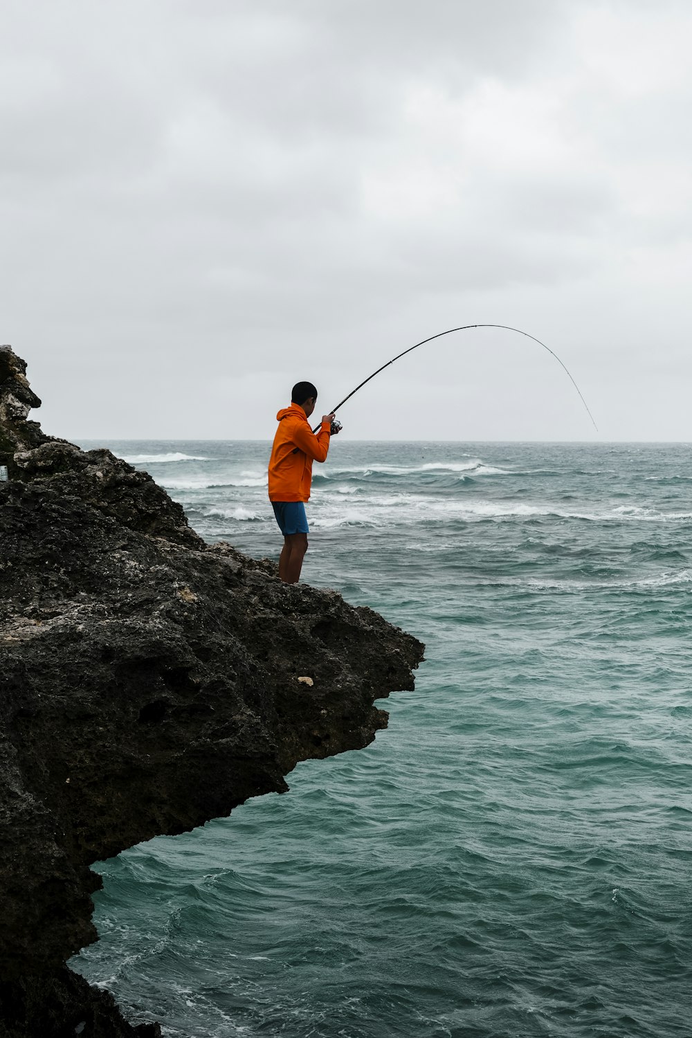 Mann in orangefarbener Jacke und blauer Jeans beim Fischen auf See tagsüber