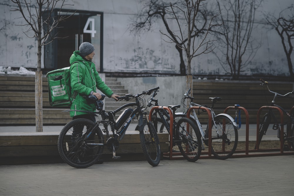 녹색 재킷과 파란색 데님 청바지를 입은 남자가 검은 자전거를 타고 있다
