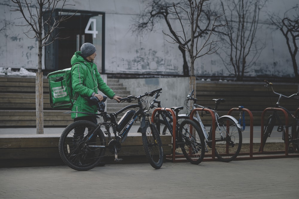 man in green jacket and blue denim jeans riding on black bicycle