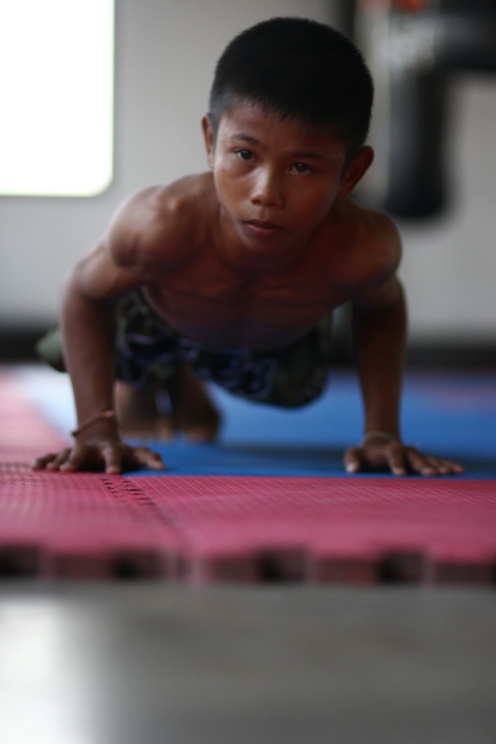 topless man in blue and white shorts kneeling on red mat