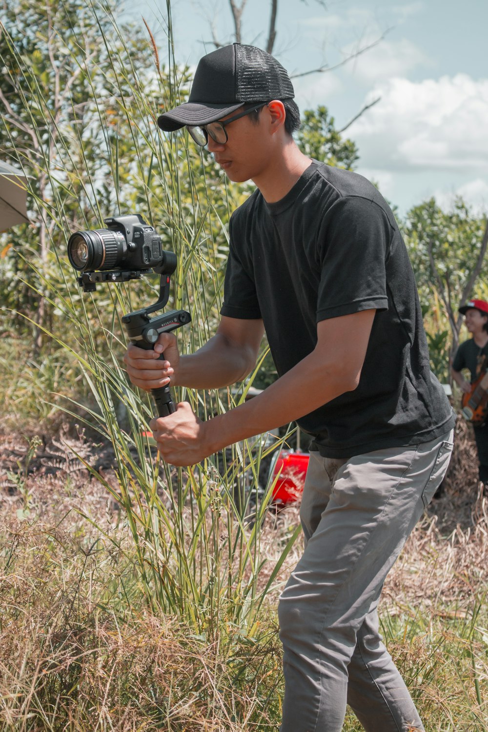 Hombre con camiseta negra de cuello redondo y pantalones grises sosteniendo una cámara DSLR negra