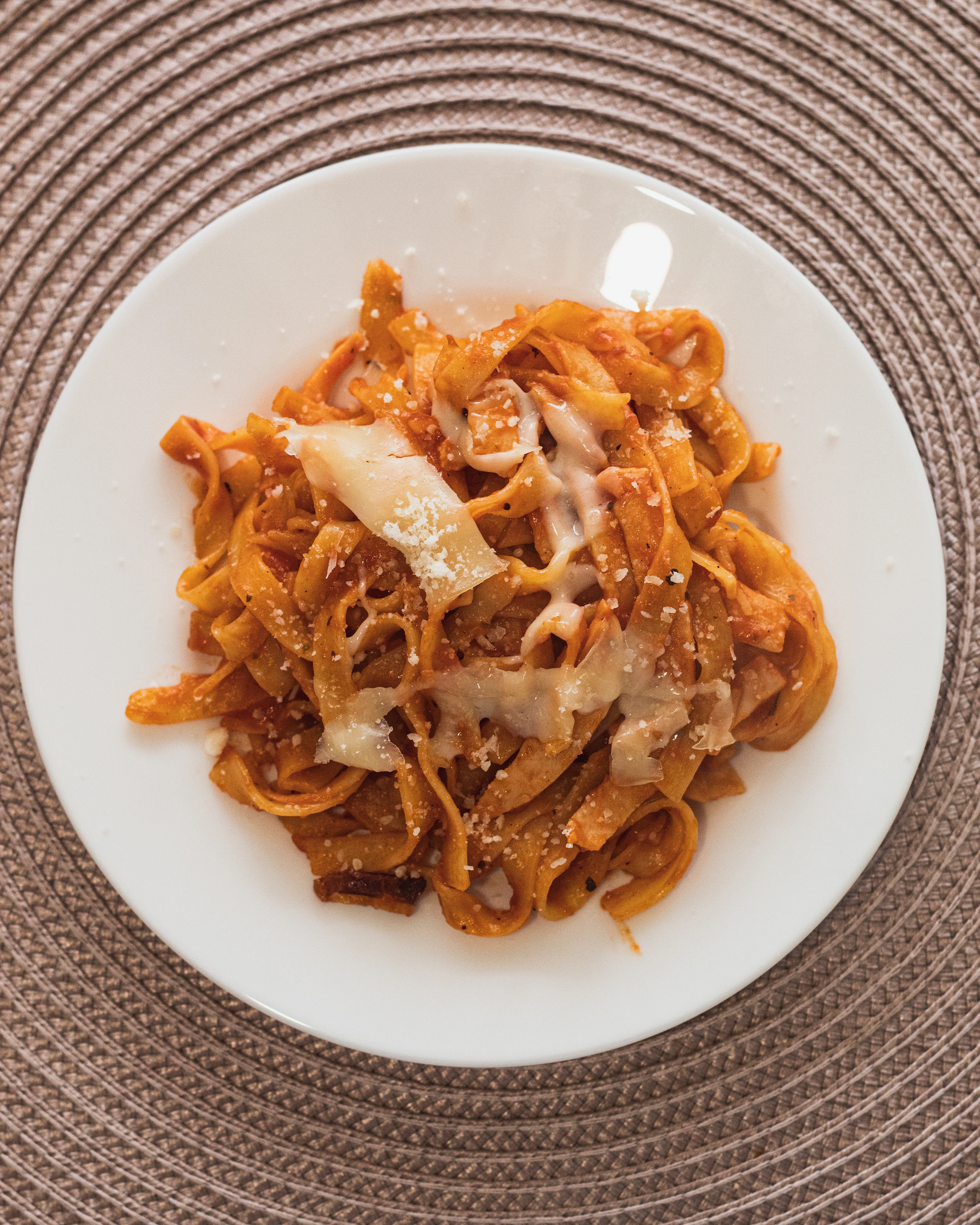 A steaming plate of handmade pasta topped with rich, red tomato sauce and sprinkled with parmesan cheese.