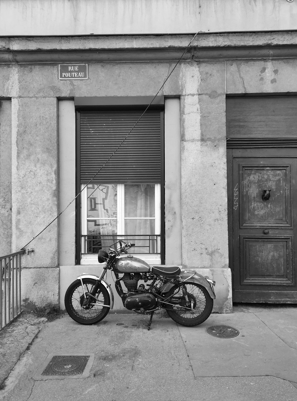 grayscale photo of motorcycle parked beside building