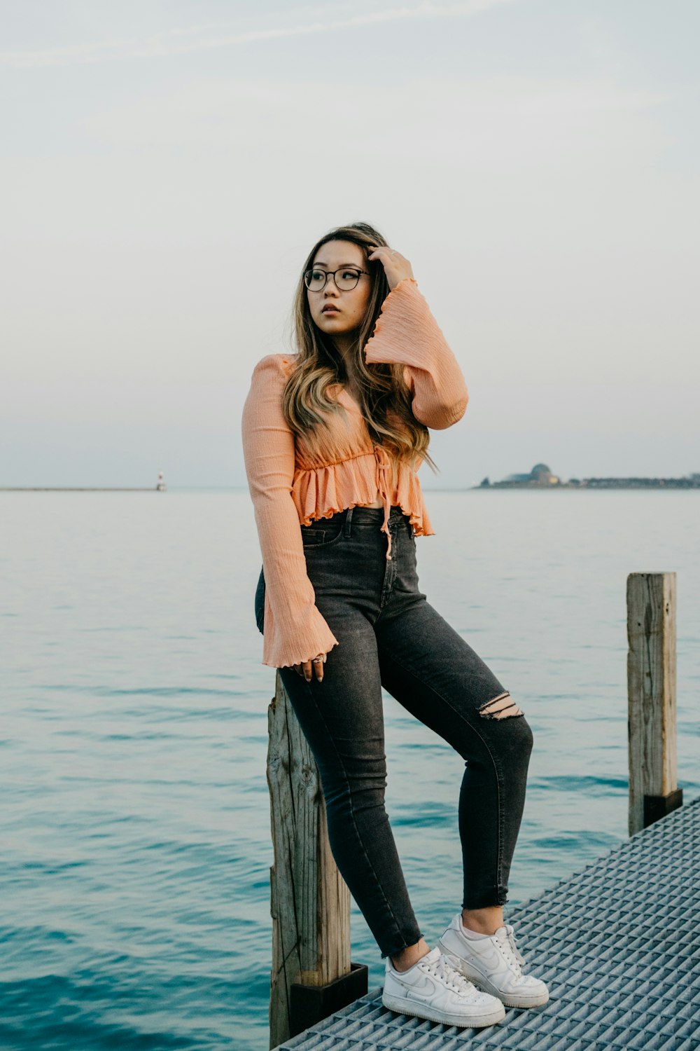 Mujer con camisa marrón de manga larga y jeans vaqueros azules de pie en el muelle durante el día