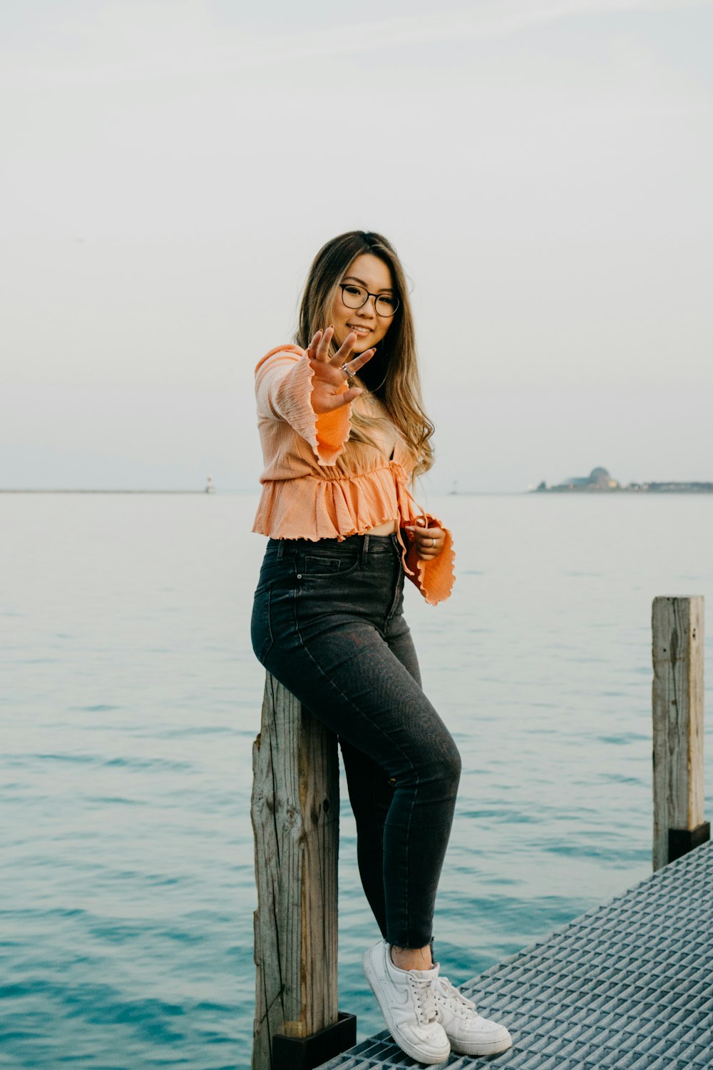 woman in pink long sleeve shirt and blue denim jeans sitting on brown wooden post