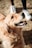 A joyful, golden-hued dog looks upwards with a happy and expectant expression. The sunlight illuminates its fur, highlighting its wavy texture. Nearby, a pair of white sneakers suggests the presence of a person holding the dog's leash.
