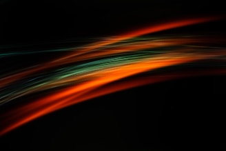 Abstract light trails with a combination of orange and green hues on a dark background, creating a dynamic and fluid motion effect.