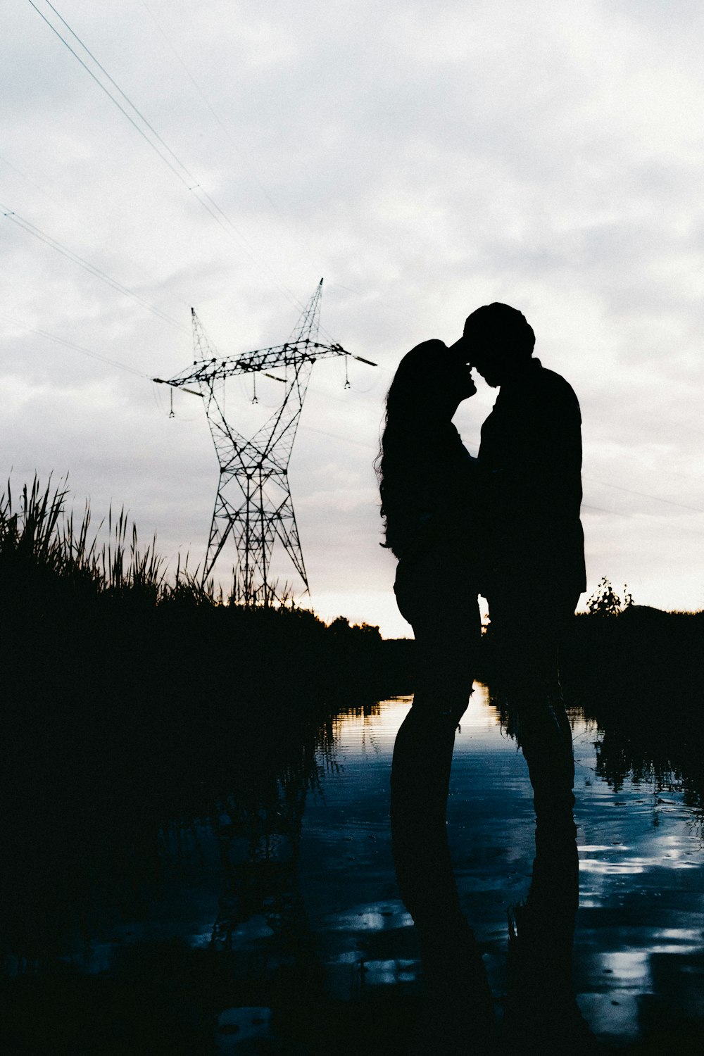 silhouette of man and woman standing near body of water during daytime