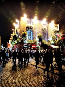 A dynamic city street scene at night with groups moving between pubs, glowing with warm lights and buzzing energy.