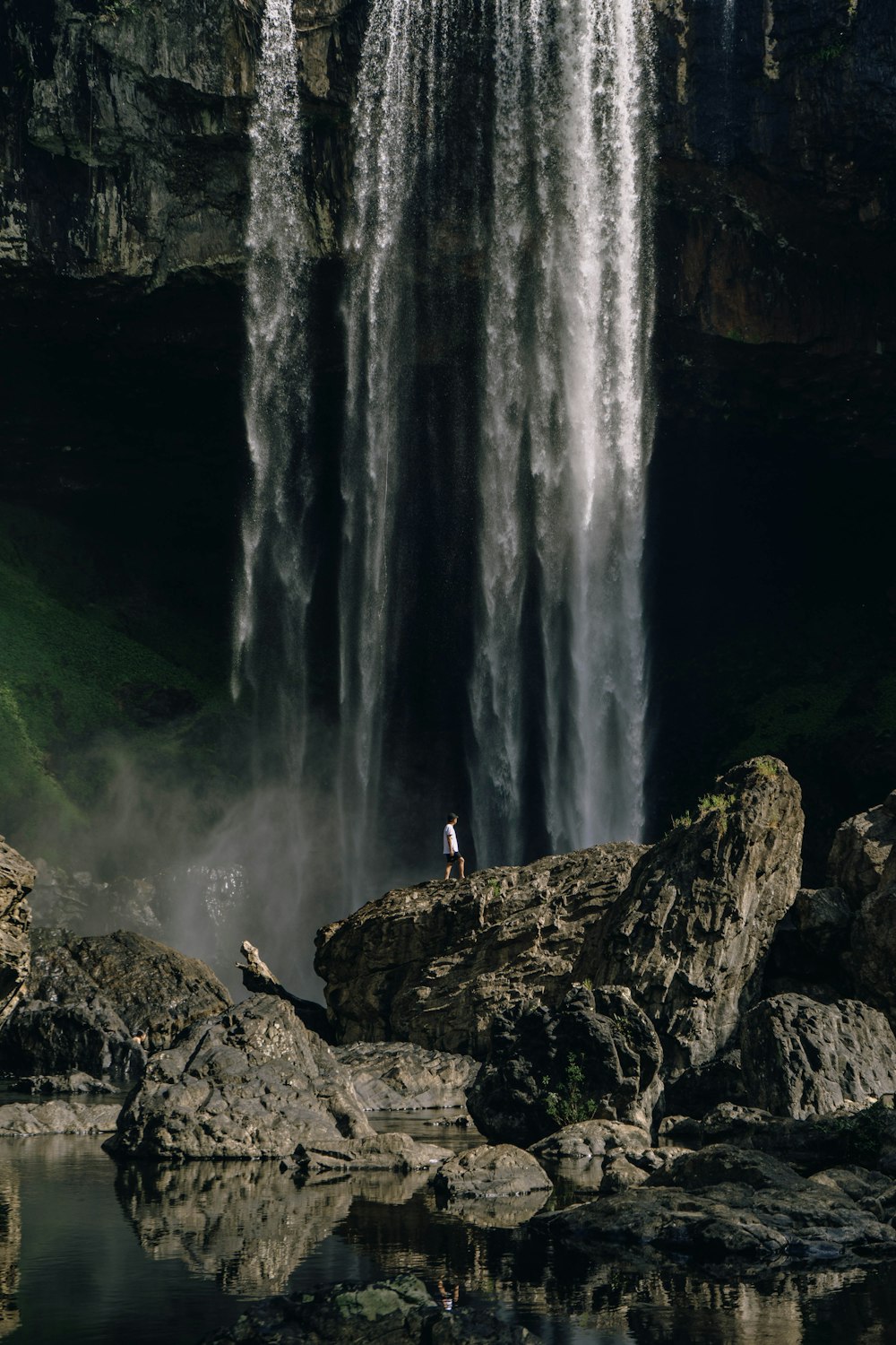 man standing on rock near waterfalls during daytime