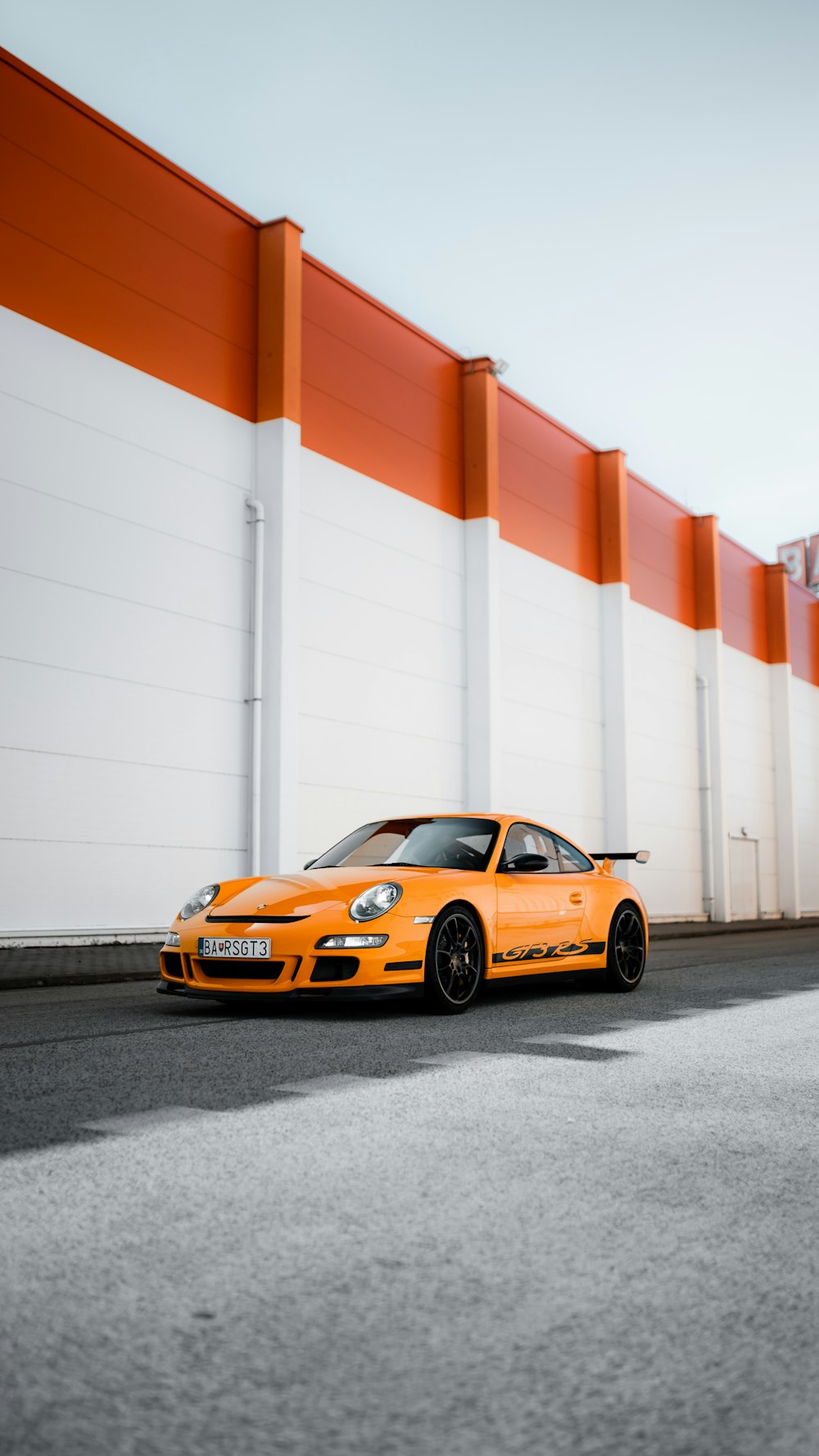 Porsche 911 naranja y negro aparcado junto a la pared blanca y roja