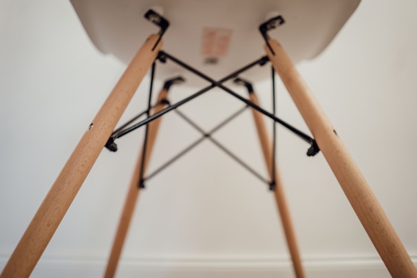 A close-up view of the underside of a chair, focusing on the wooden legs and metal supports. The legs are light-colored wood with a smooth finish, connected by black metal rods forming a geometric pattern.