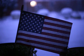 A close-up of a police badge with the American flag blurred in the background, symbolizing ICE activity.