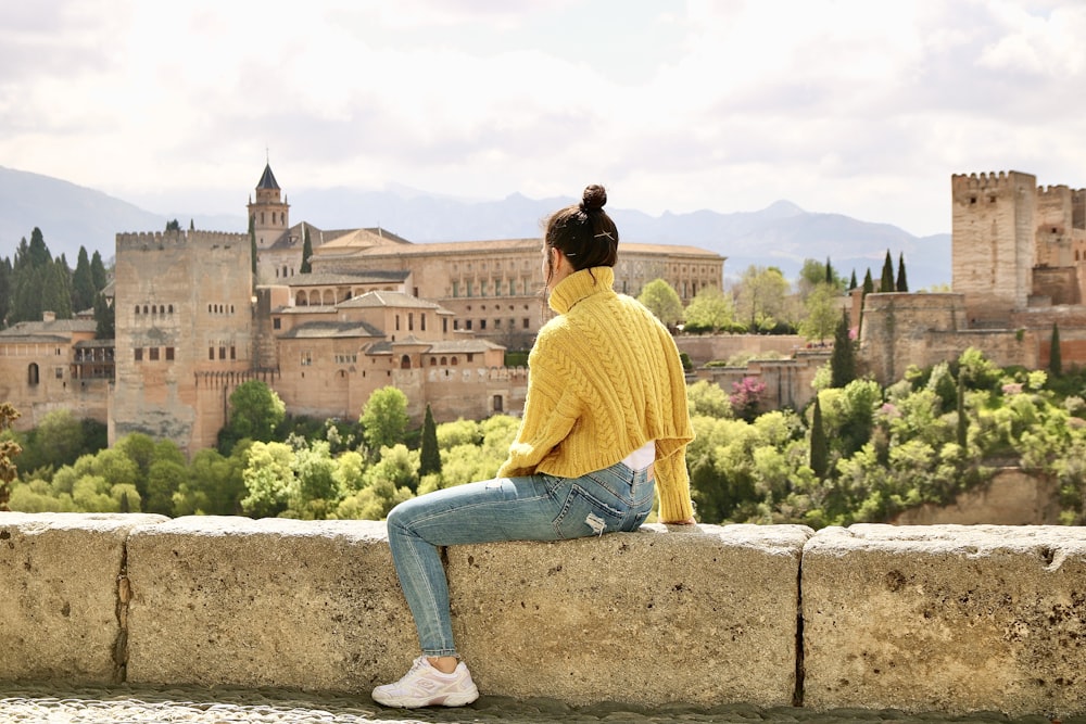 man in yellow long sleeve shirt and blue denim jeans sitting on concrete bench during daytime