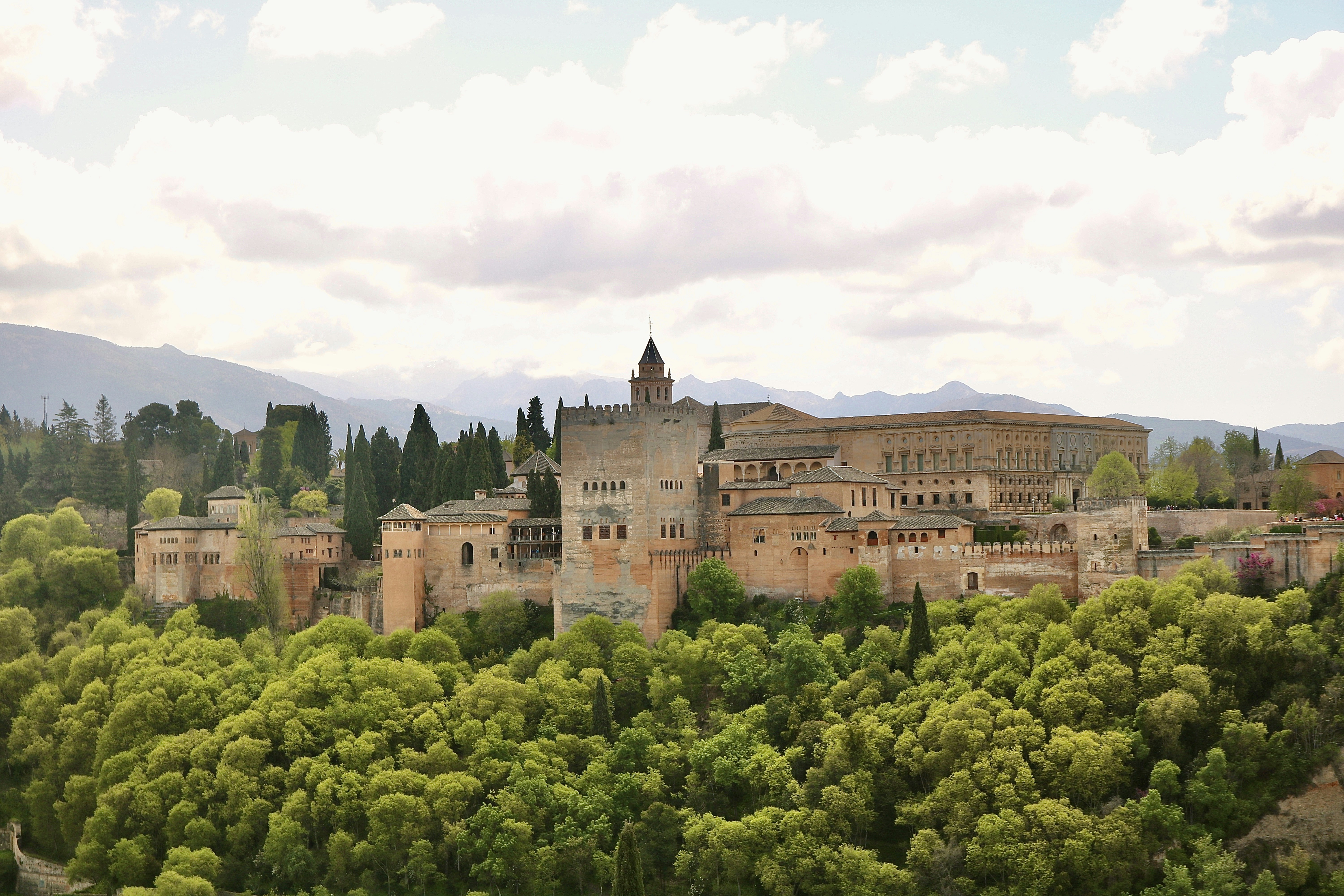 brown concrete building near green trees under white clouds during daytime
