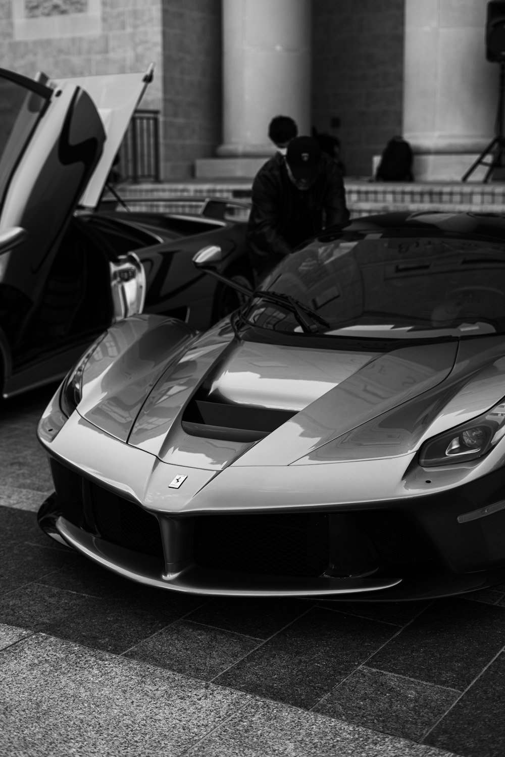 grayscale photo of man standing beside car