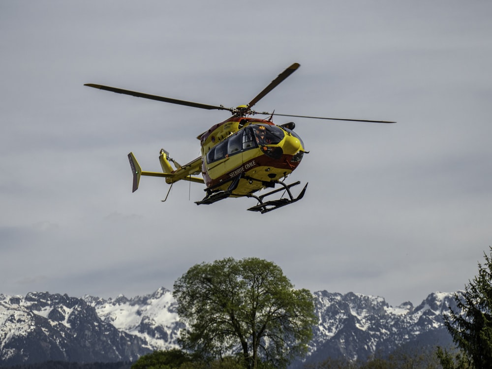 yellow and black helicopter flying over snow covered mountain during daytime