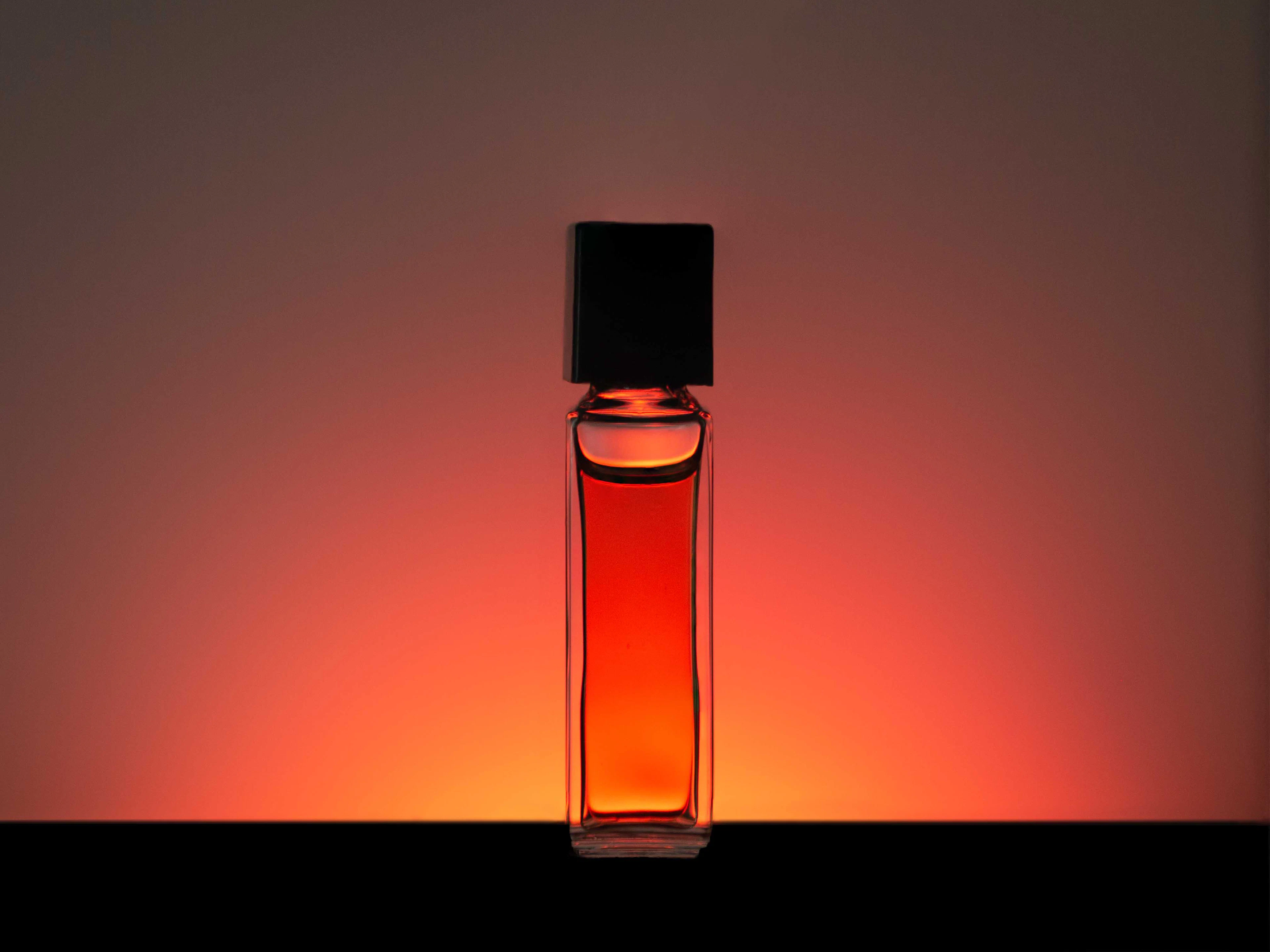 Frasco de perfume ámbar iluminado con un degradado cálido (imagen ilustrativa)