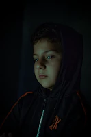 Cinematic shot of a model wearing a black oversized hoodie with glowing red accents against a smoky black gradient background.