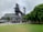 An industrial structure, possibly part of a historic steel mill, stands prominently with a mix of modern design elements. The area around it includes green trees and a well-maintained lawn. The sky appears overcast, contributing to a subdued atmosphere.