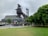 An industrial structure, possibly part of a historic steel mill, stands prominently with a mix of modern design elements. The area around it includes green trees and a well-maintained lawn. The sky appears overcast, contributing to a subdued atmosphere.