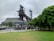 An industrial structure, possibly part of a historic steel mill, stands prominently with a mix of modern design elements. The area around it includes green trees and a well-maintained lawn. The sky appears overcast, contributing to a subdued atmosphere.
