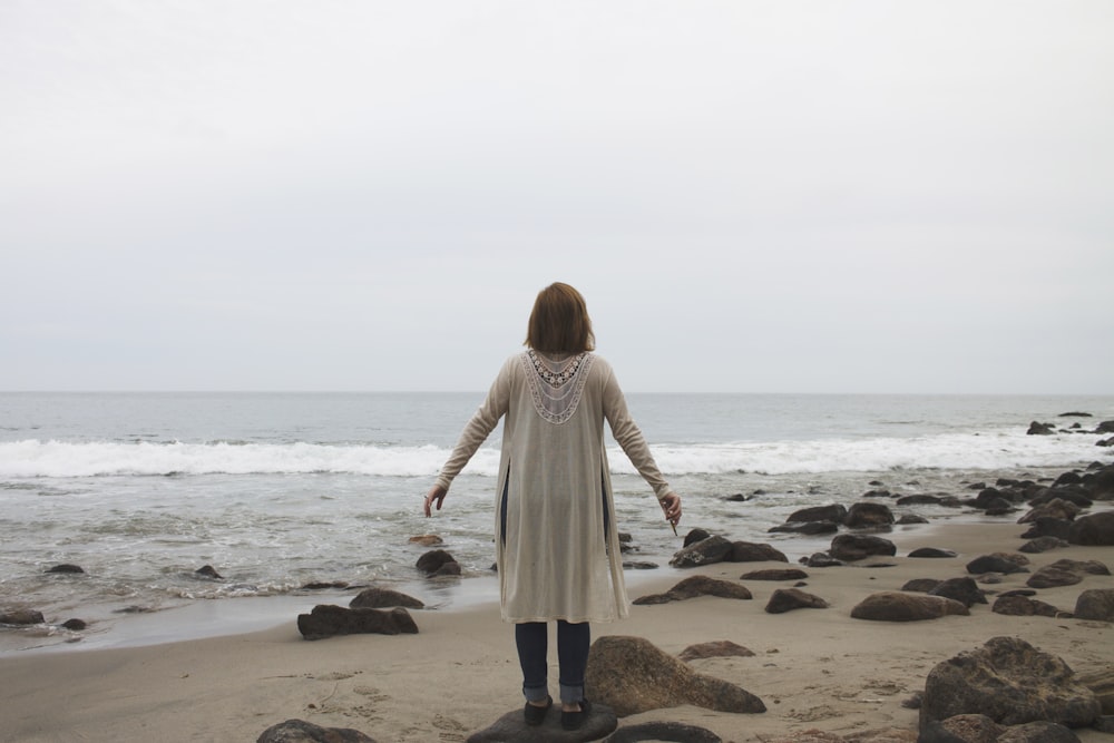 mulher no vestido branco da manga comprida que está em pé na praia durante o dia