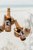 Smiling friends clinking glasses of cold drinks on a sunny beach.