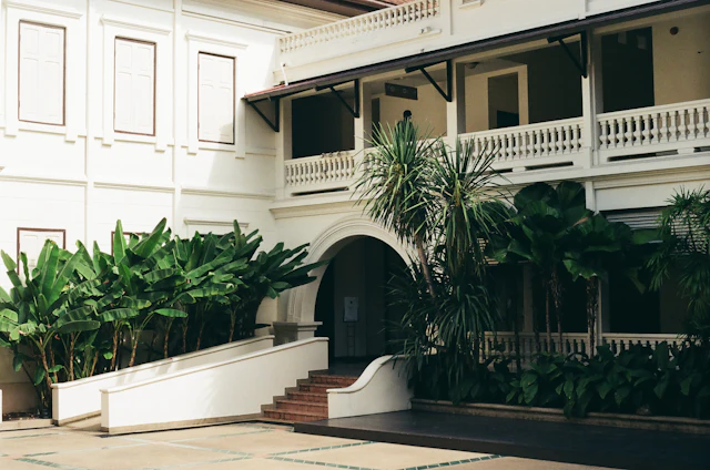 The white colonial-era courtyard and balustraded balconies of the Museum Siam building, framed by tropical plants.