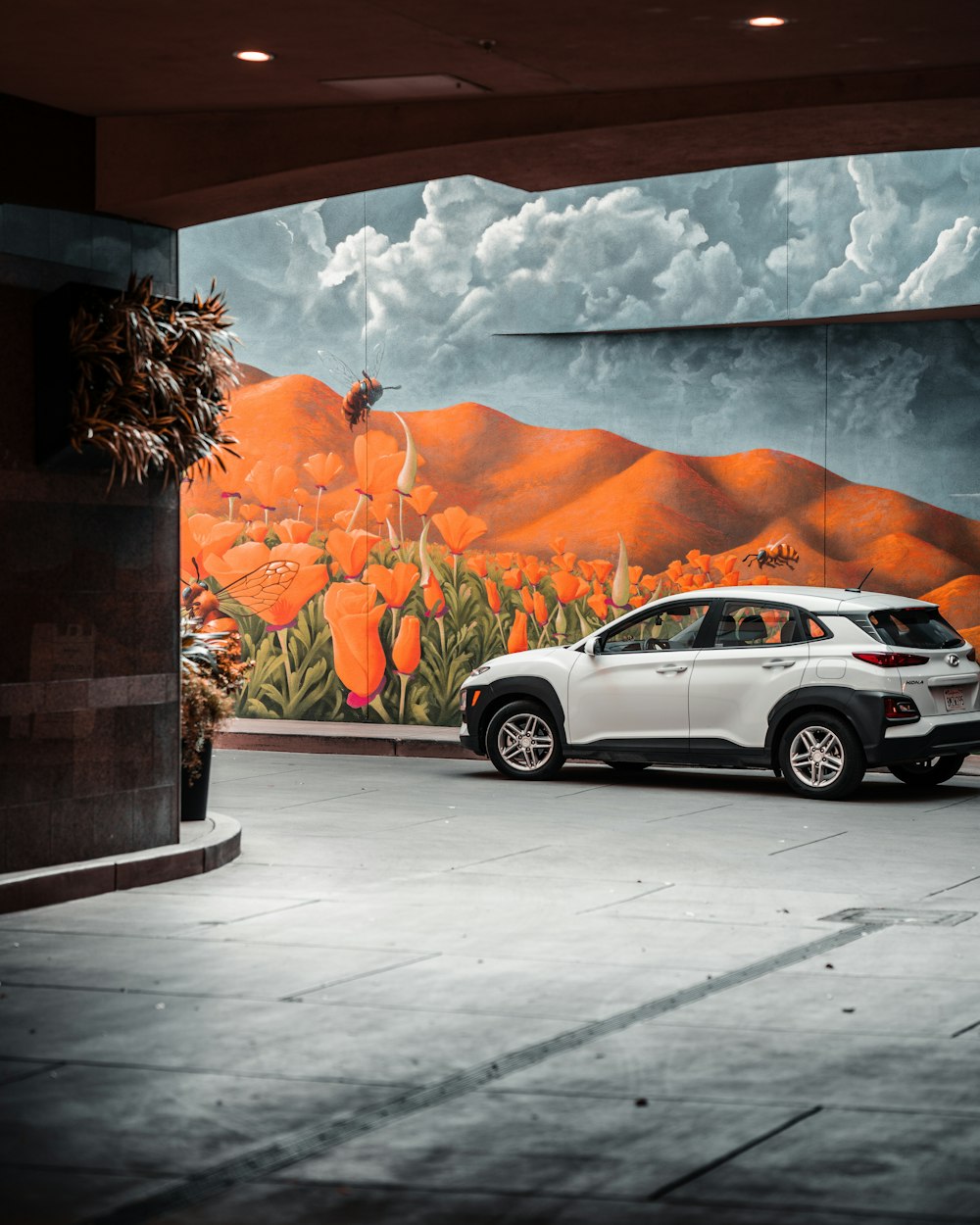 silver sedan parked beside wall with painting