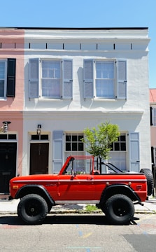 A vibrant red convertible with hand-painted accents parked on a palm-lined street.
