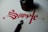 Red calligraphy spells the word 'Simple' on white paper. Next to the writing, there is a black ink jar and a calligraphy pen with a metallic nib.
