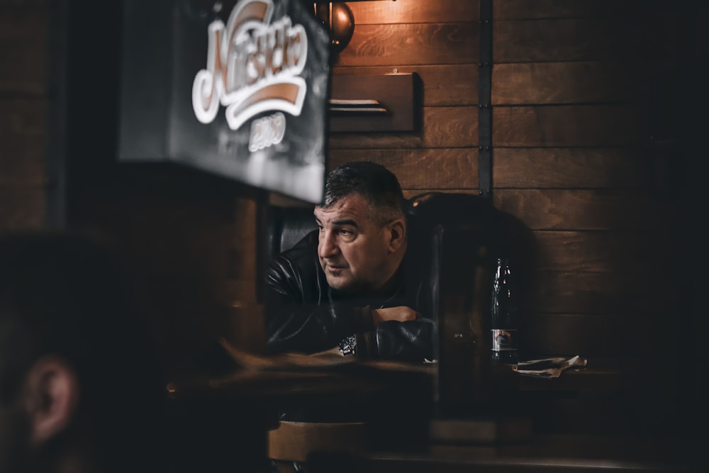 man in black leather jacket sitting beside brown wooden table