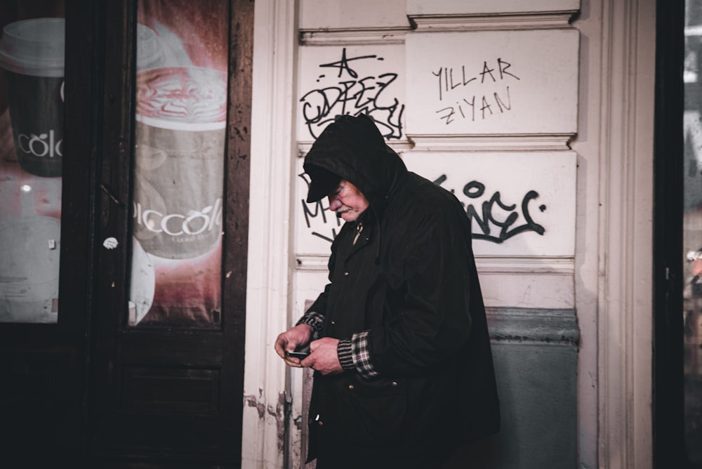 man in black hoodie standing beside white wall