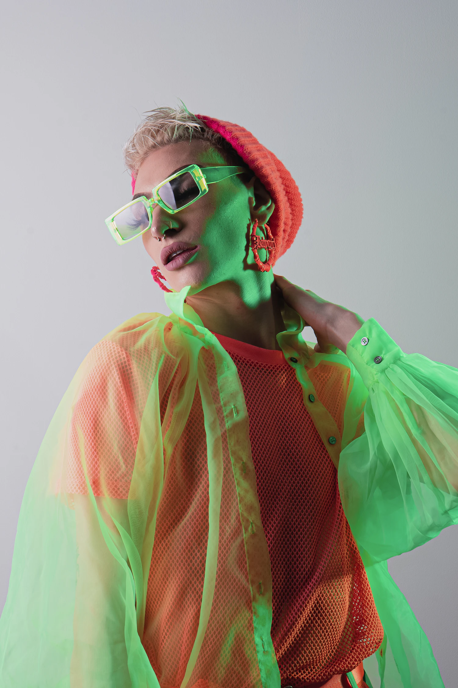 Model in a green mesh coat and oversized sunglasses against a pale seamless