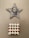 A wall-mounted star-shaped art piece features a textured net-like pattern with a ceramic face at its center. Below it is a square tile with a pattern of red hearts on a light background.