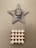 A wall-mounted star-shaped art piece features a textured net-like pattern with a ceramic face at its center. Below it is a square tile with a pattern of red hearts on a light background.