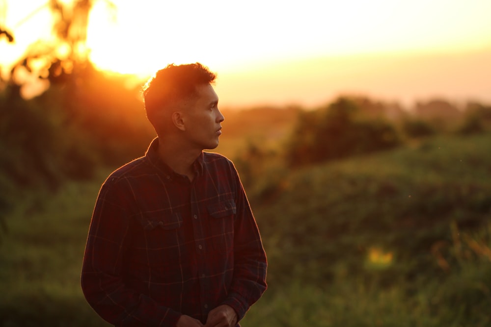 man in black and white plaid dress shirt standing on green grass field during sunset