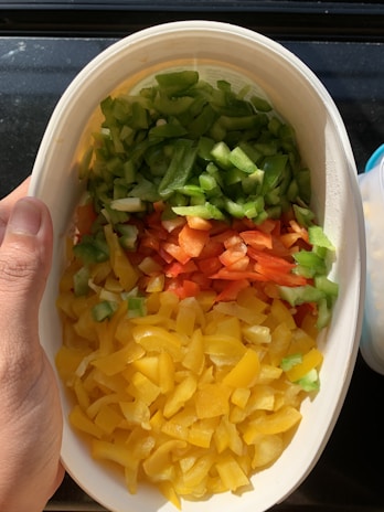 A hand holding a bowl filled with vibrant veggies and grains, sunlight highlighting the textures.