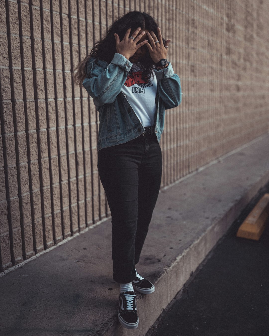 woman in blue denim jacket and black pants standing beside brown brick wall during daytime