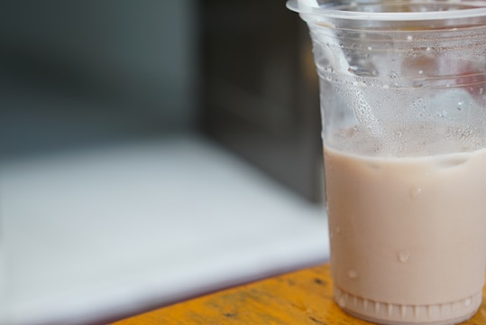 A refreshing iced drink in a transparent cafecup cup with condensation droplets, set against a sunny outdoor cafe background.