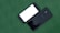 Two smartphones are placed side by side on a green surface. One phone is face down showing the brand 'Samsung,' while the other is face up with a blank white screen. Both phones are black, with sleek and shiny finishes.