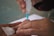 A close-up of hands using a small medical device with a blue tip to perform a procedure on a fingertip. A cotton pad is held nearby, suggesting a medical or testing context.