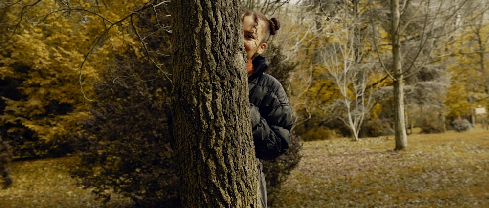 man in black jacket leaning on tree