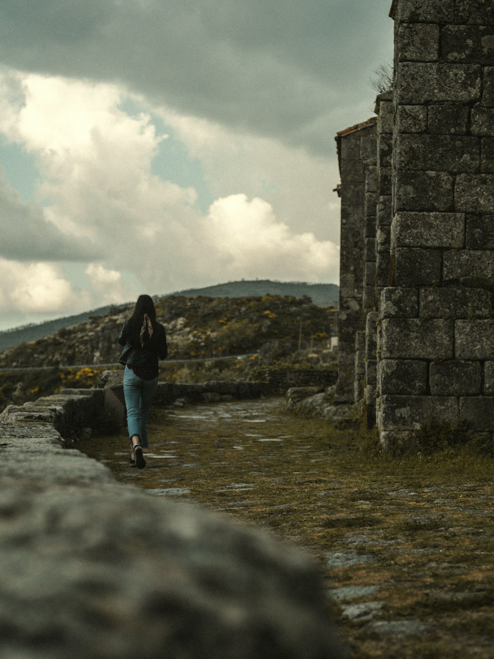 woman in black jacket and blue denim jeans standing on gray concrete bridge during daytime