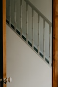 A wooden door is partially open, revealing a white staircase with evenly spaced spindles. The wall beside the staircase is painted white, creating a simple and clean interior look.