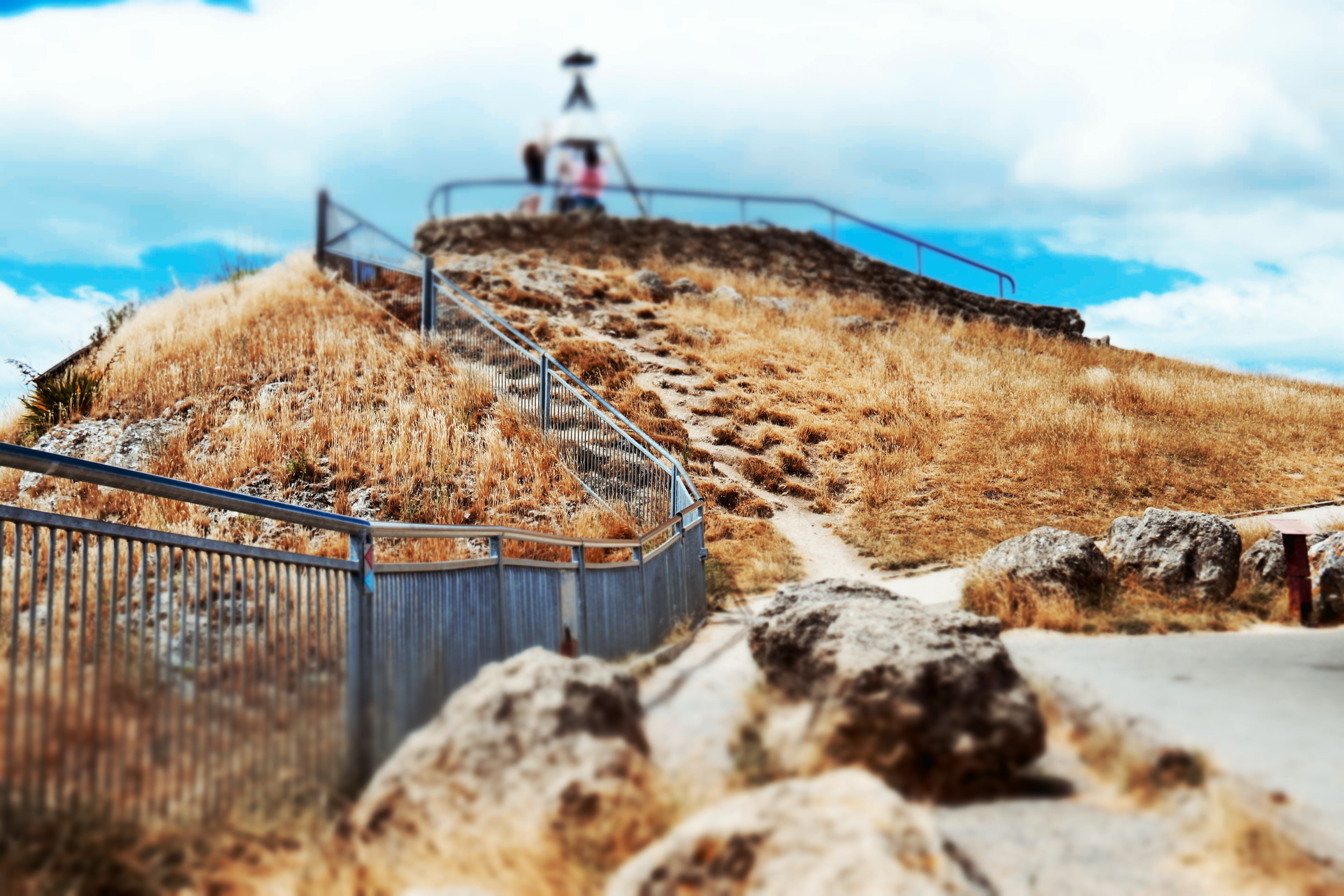 man in white shirt standing on brown rock near blue metal fence during daytime